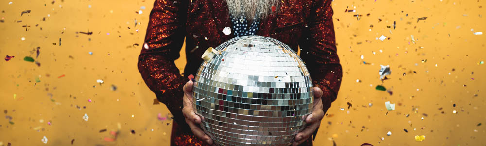 Close-up of hands of an old man holding a disco ball, with confetti falling behind him